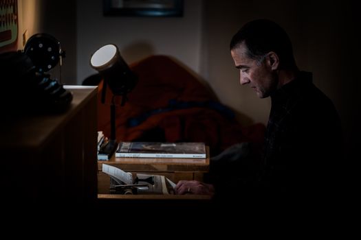Side view of a man typing on a vintage typewriter in a dimly lit indoor workspace.