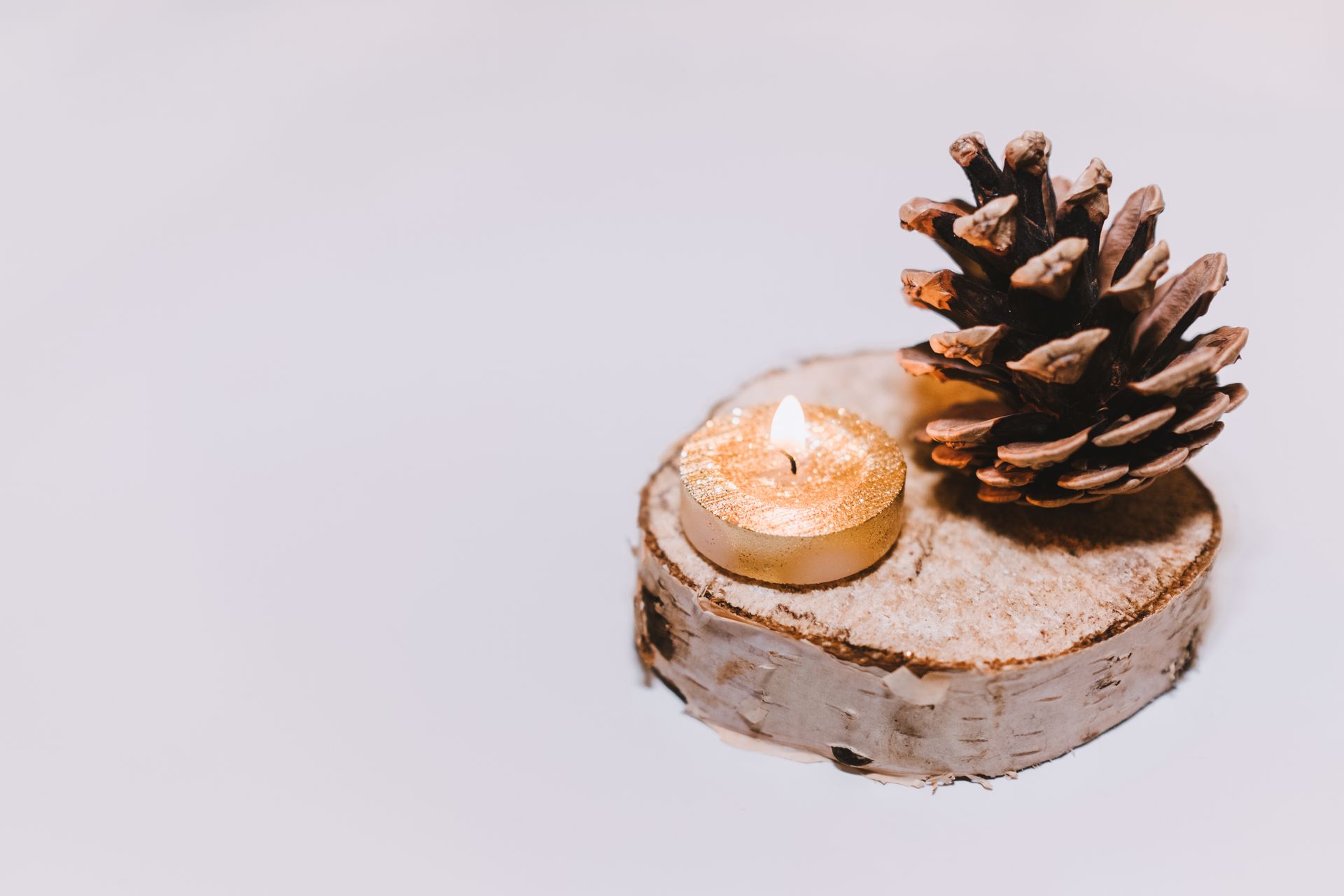 Warm candlelight illuminating a pine cone on a rustic birch slab, perfect for winter decor.
