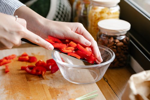 Free Crop woman putting cut bell pepper in bowl Stock Photo