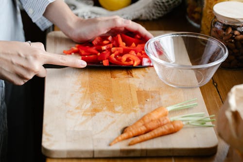 Crop unrecognizable woman cutting bell pepper in kitchen