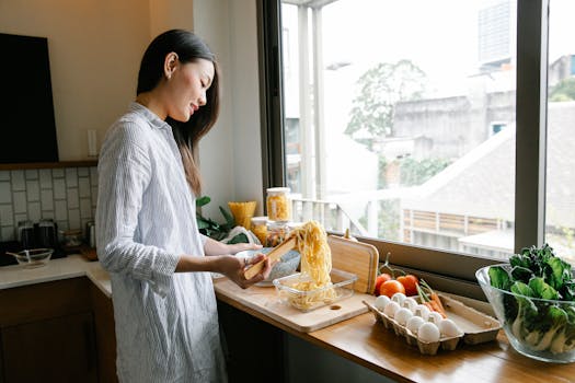 A woman preparing pasta with fresh vegetables in a cozy kitchen setting.