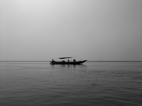 A serene black and white image of a boat and people on calm waters, showcasing peaceful solitude.