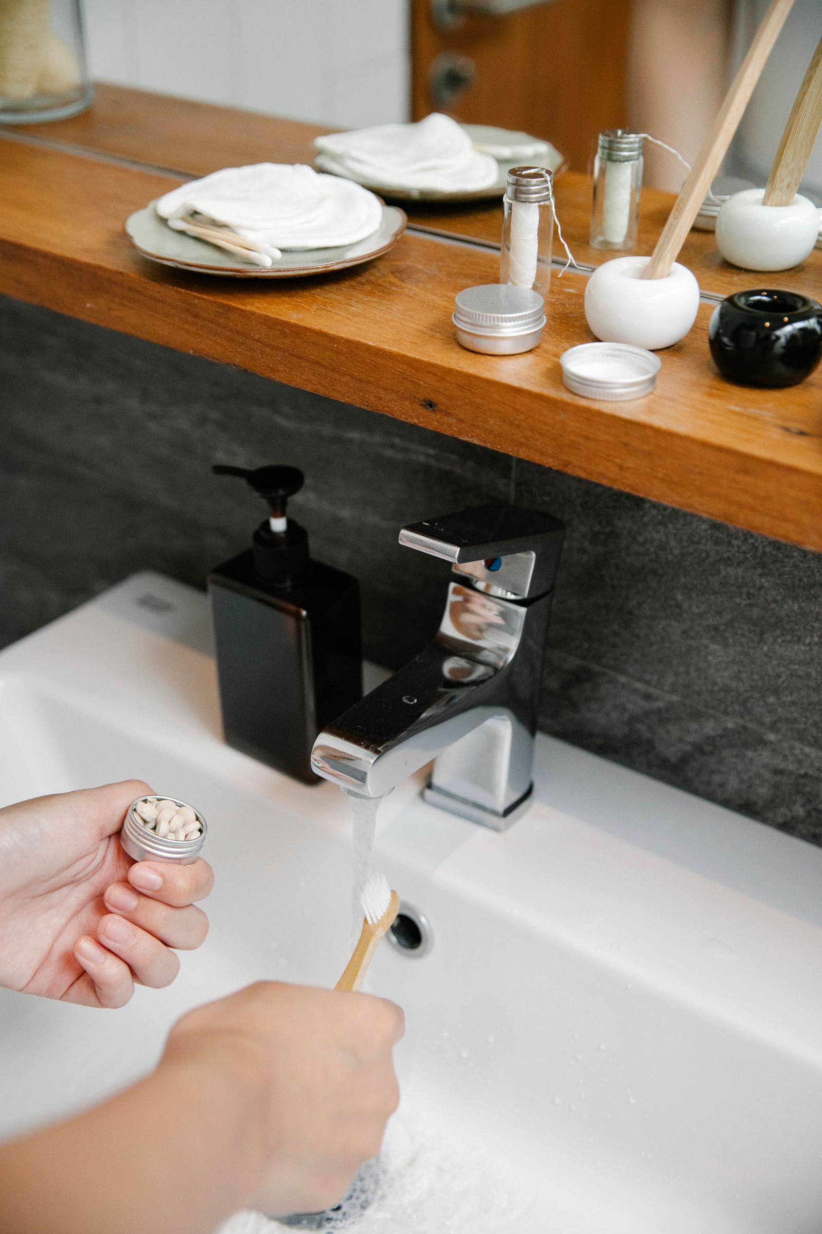 Hand preparing a bamboo toothbrush near a bright bathroom sink for a daily oral-care routine