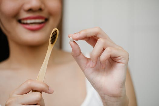 Smiling woman holding a bamboo toothbrush and a toothpaste tablet, promoting eco-friendly oral hygiene.