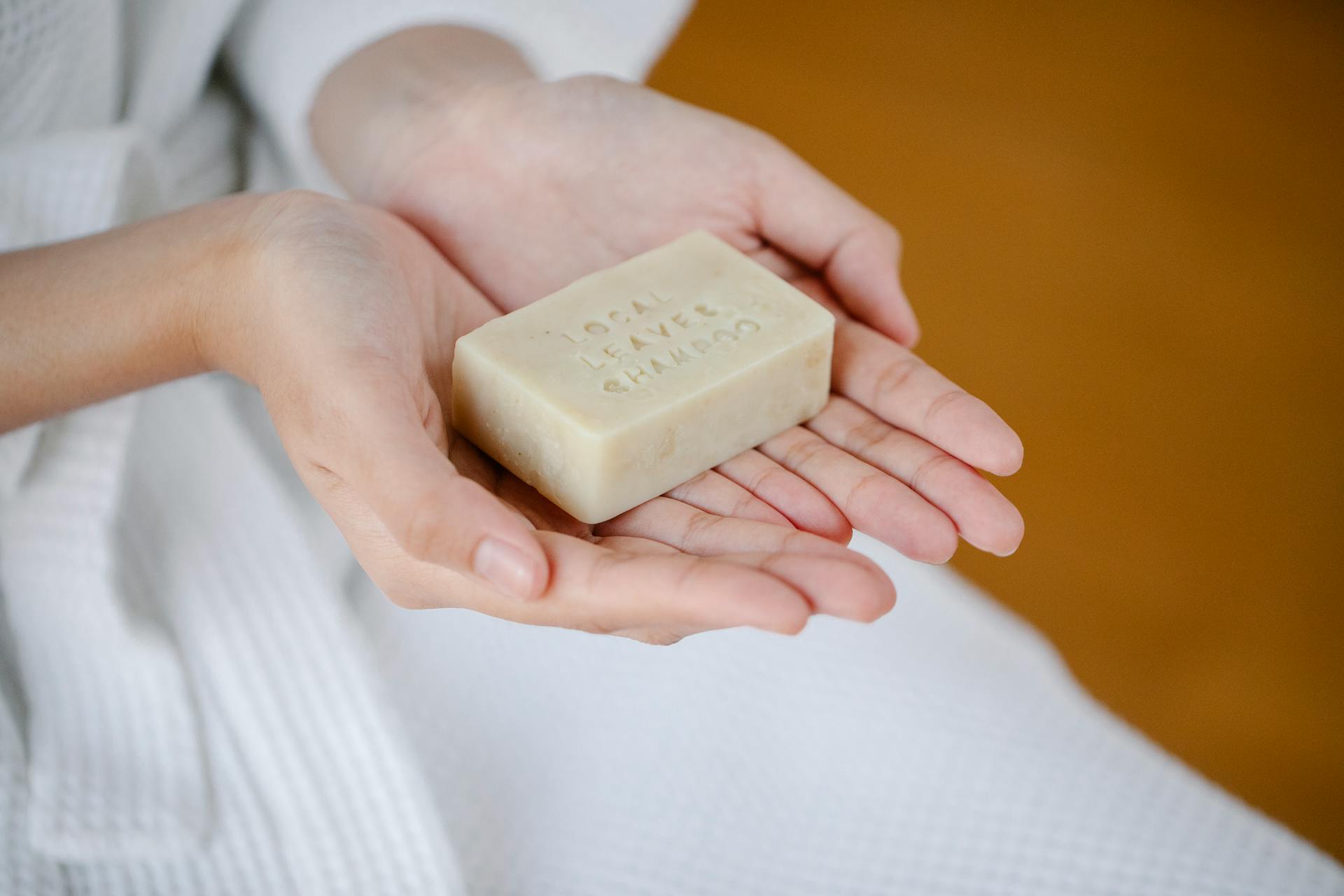 Crop anonymous female showing rectangular shaped dry ecological shampoo with title on blurred background