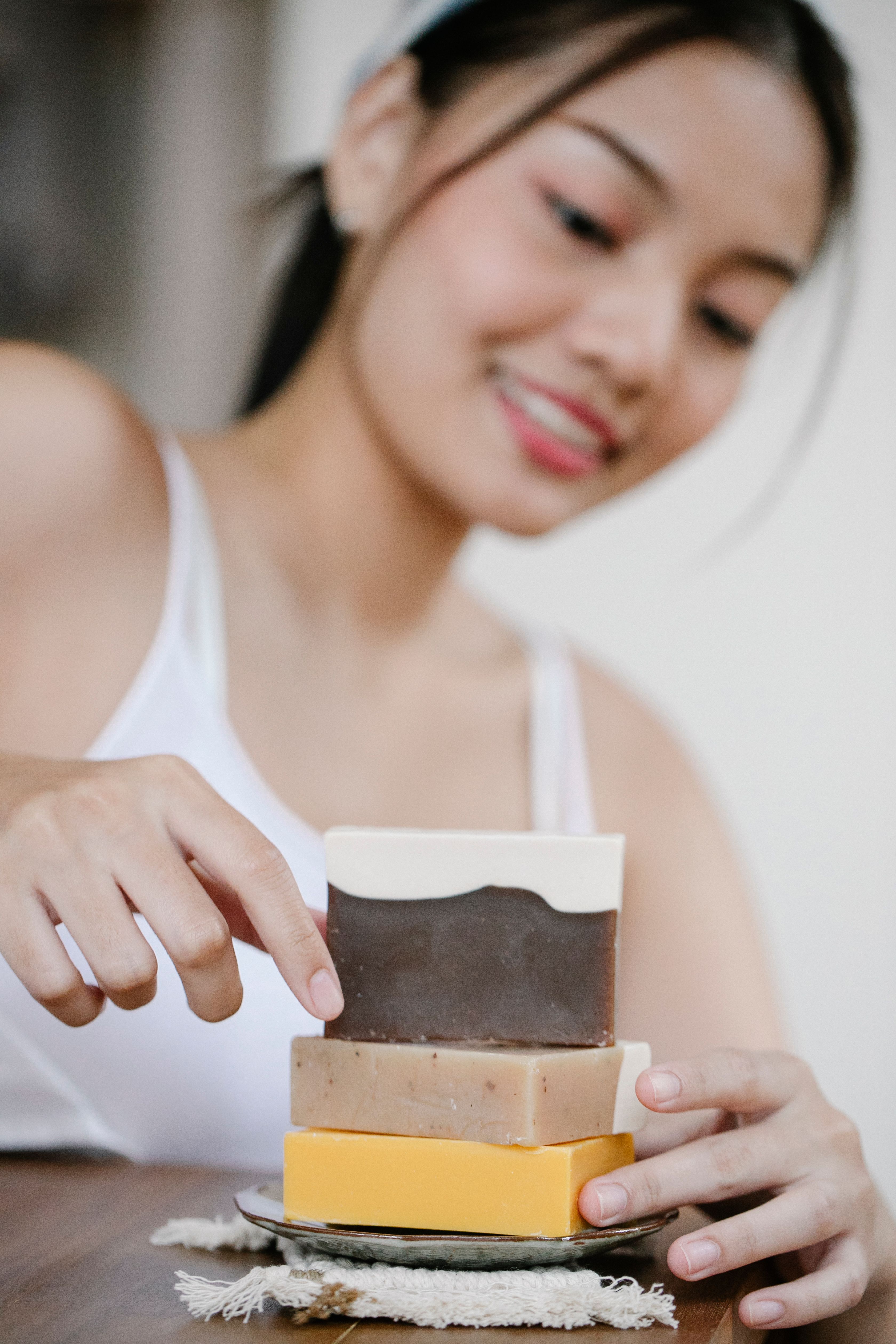 Positive Asian female with collection of colorful ECO soap for daily skin care routine placed on table in light room