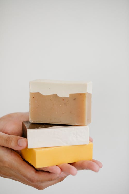 Unrecognizable person demonstrating abundance of colorful ECO soap on hand for skin care routine on white background in light room