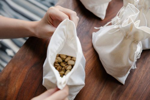 Free From above crop unrecognizable person showing white recycling bag with pistachios at wooden table near other white bags Stock Photo