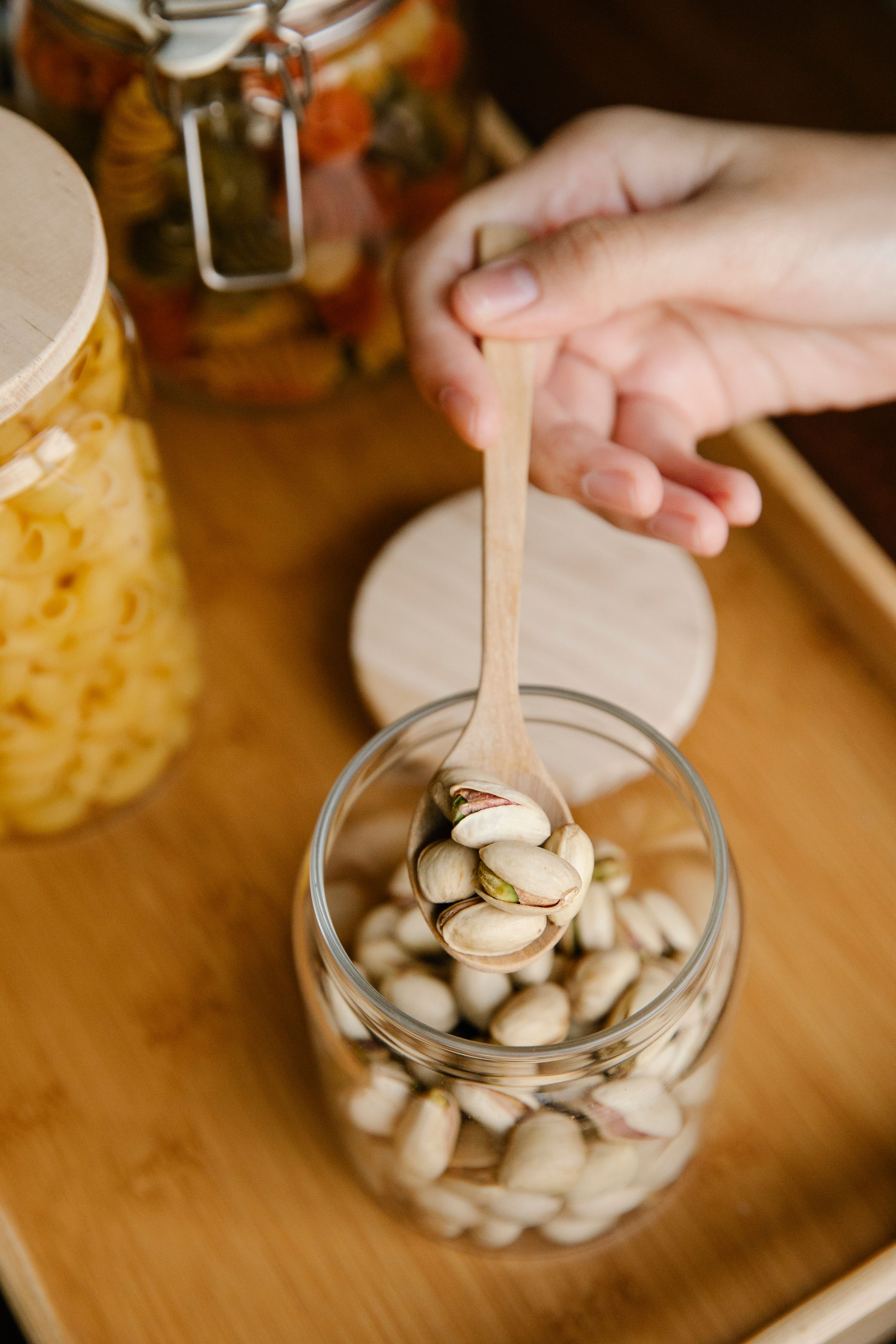 From above of crop anonymous person taking spoon with pistachios from glass jar on wooden table - how to store dry fruits