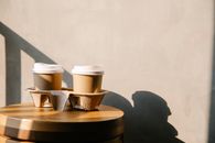 Cofee paper cups with plastic lids on holder tray on brown wooden table casting a shadow at sunny day