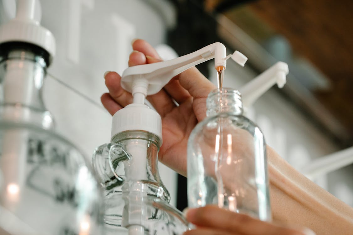 Free Crop unrecognizable person pushing and pouring soap from dispenser to plastic bottle Stock Photo