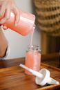 Crop anonymous person standing at table with opened soap dispenser and pouring peach coloured soap into bottle