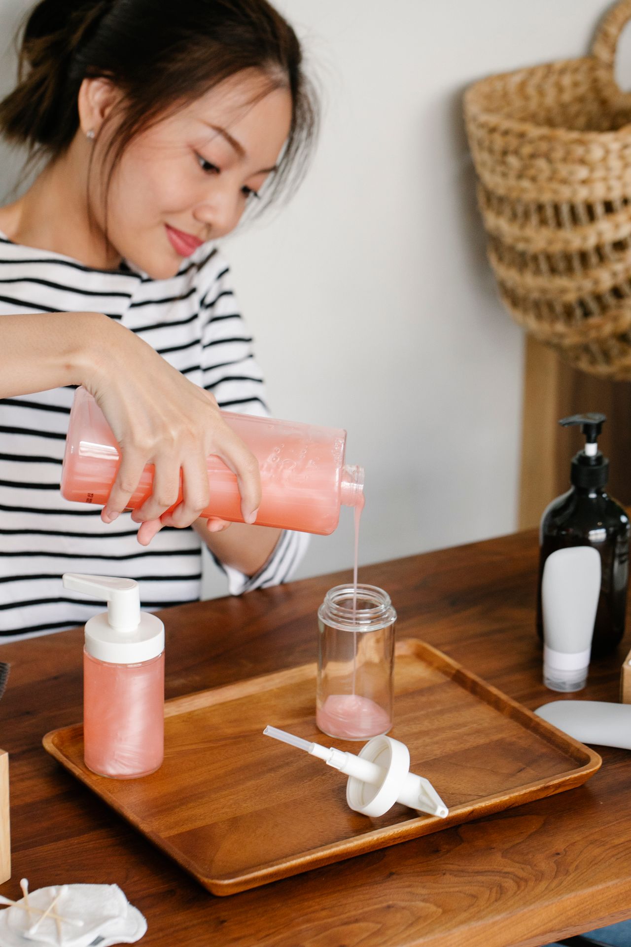 Person pouring pink liquid soap from a large bottle into a smaller refillable bottle