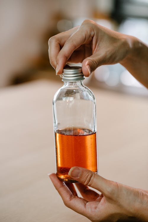 Personne Tenant Une Bouteille En Verre Transparent Avec Un Liquide Brun