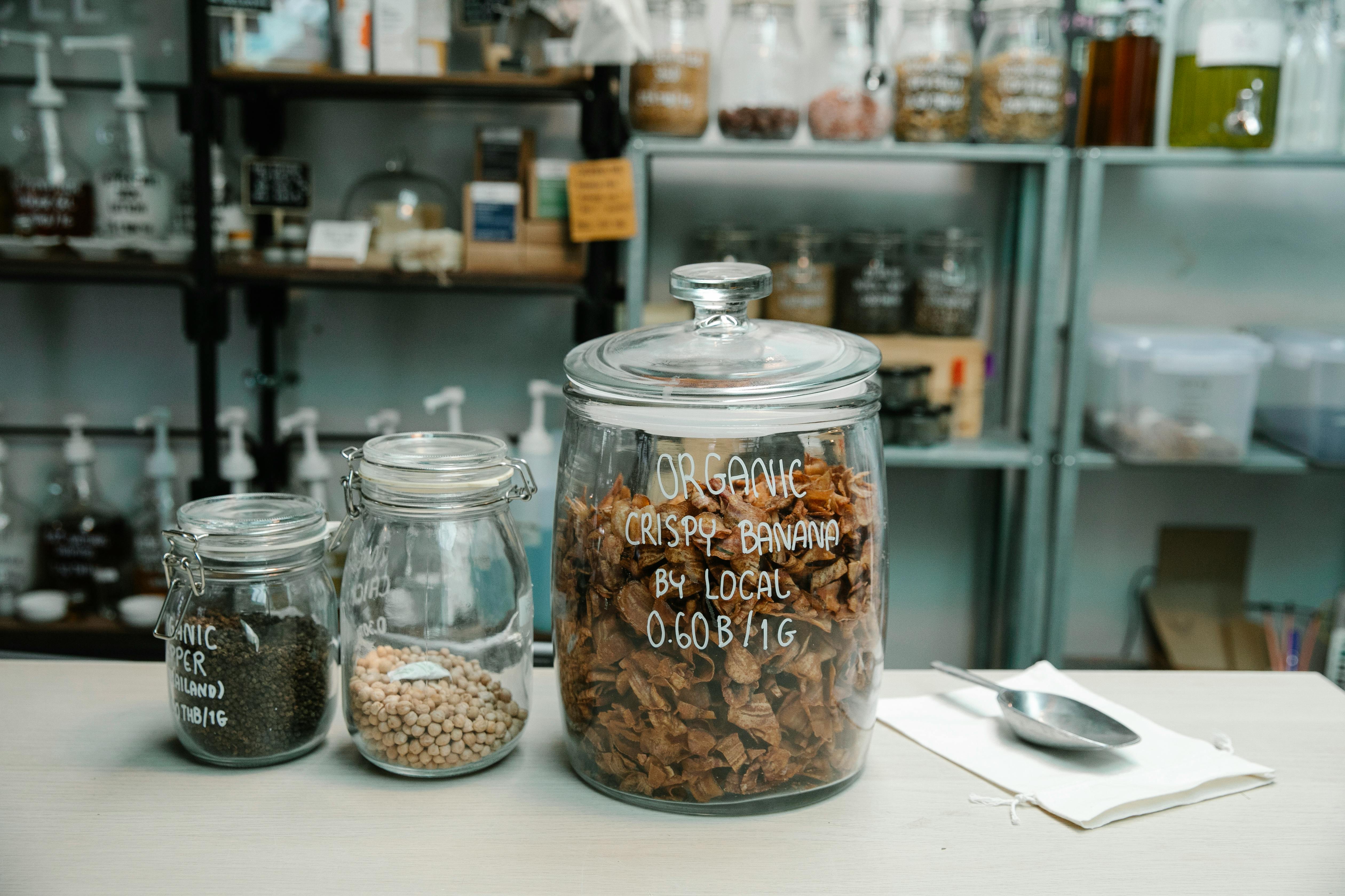 Close-up of organic dried banana chips in a glass jar on a kitchen countertop with ingredients.