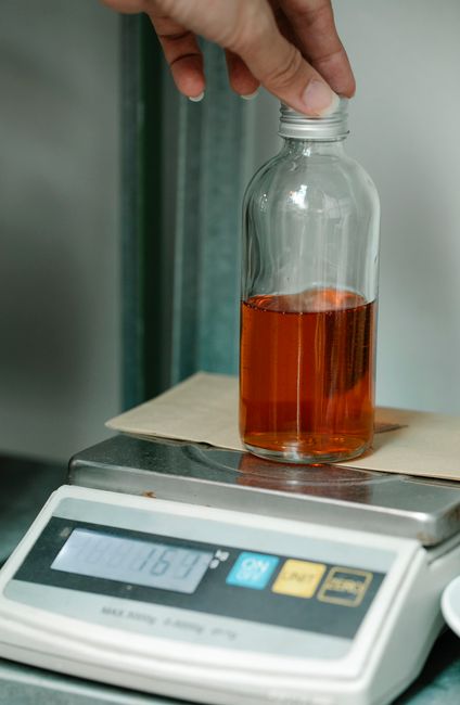 A small glass bottle filled with thick, dark brown caramel color liquid, with a few drops pooled on a spoon beside it to show the syrupy texture