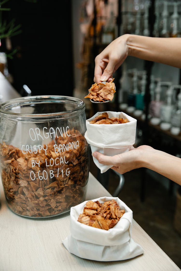 A Person Putting Organic Banana Chips In A White Bag