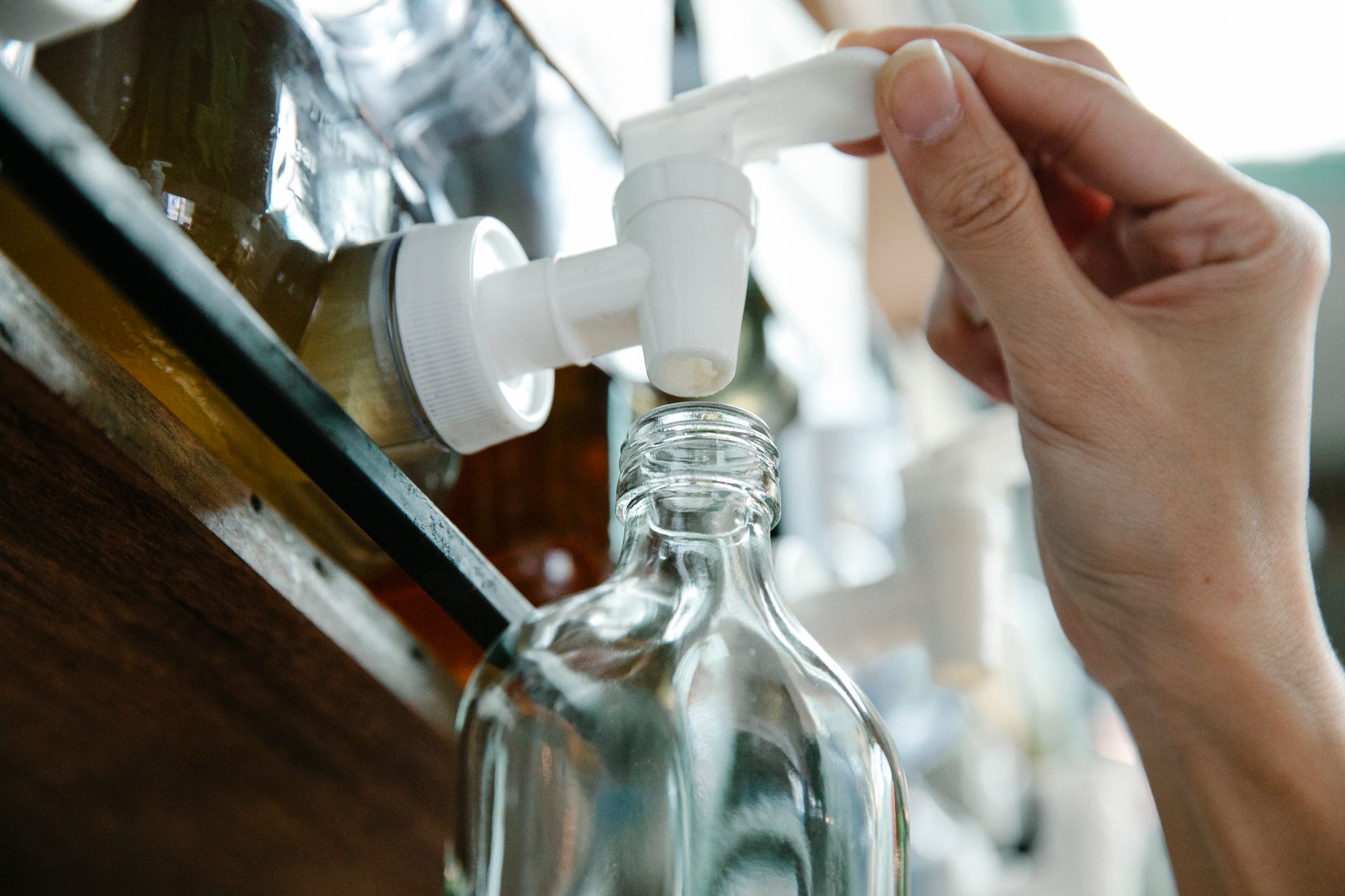 Close-up of a hand refilling a glass bottle from a liquid dispenser with a pump in an eco-friendly setup.