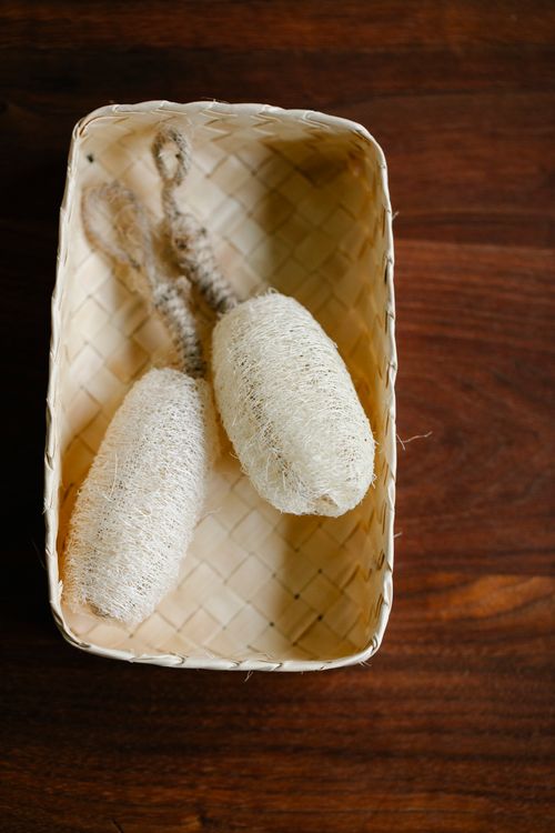 Free Two natural loofah sponges in a woven basket on a wooden surface. Stock Photo