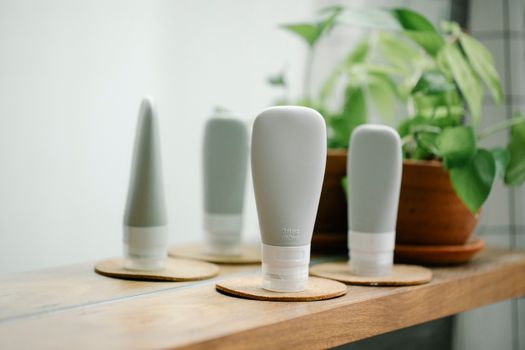 Gray tubes with skincare products placed on coasters on wooden shelf near mirror in light room with green potted plant