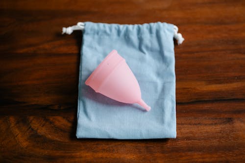 Top view of pink menstrual cup for feminine hygienic procedure on cloth bag placed on wooden table in light room