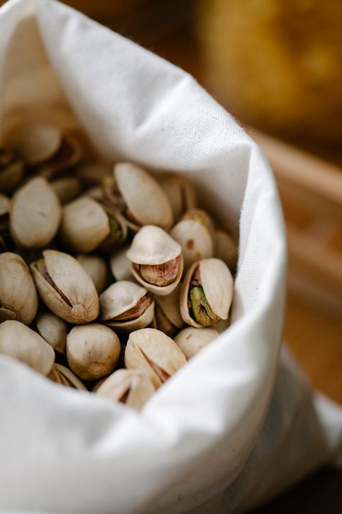 Free From above abundance of ripe pistachios in white ECO friendly sack placed on table in light room on blurred background Stock Photo