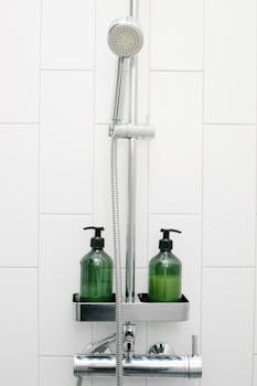 Chic modern shower setup with green dispenser bottles and chrome fixtures in a white tiled bathroom.