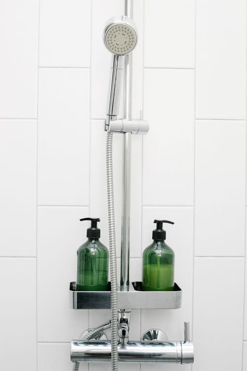 Free Handshower and hose attached to white tiled wall near bottles with essential skin care products in light bathroom Stock Photo