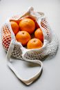 From above heap of whole ripe healthy bright oranges placed in cotton string bag on white background in light room