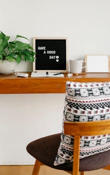 Chair with colorful cushion placed near wooden shelf with blackboard with Have A Good Day inscription near potted plant in room