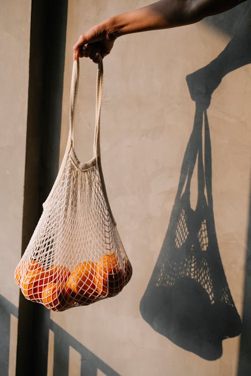 a reusable cotton bag full of oranges with it's shadow cast on a wall