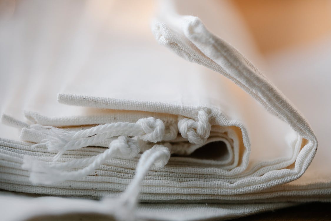 Free Pile of folded white cotton bags with ropes made of ecological cloth placed on table in light room on blurred background Stock Photo