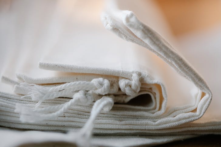Pile of folded white cotton bags with ropes made of ecological cloth placed on table in light room on blurred background