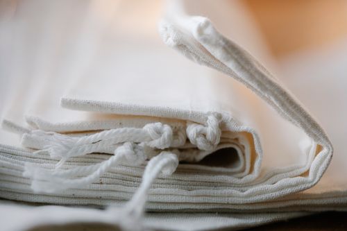 Free Pile of folded white cotton bags with ropes made of ecological cloth placed on table in light room on blurred background Stock Photo