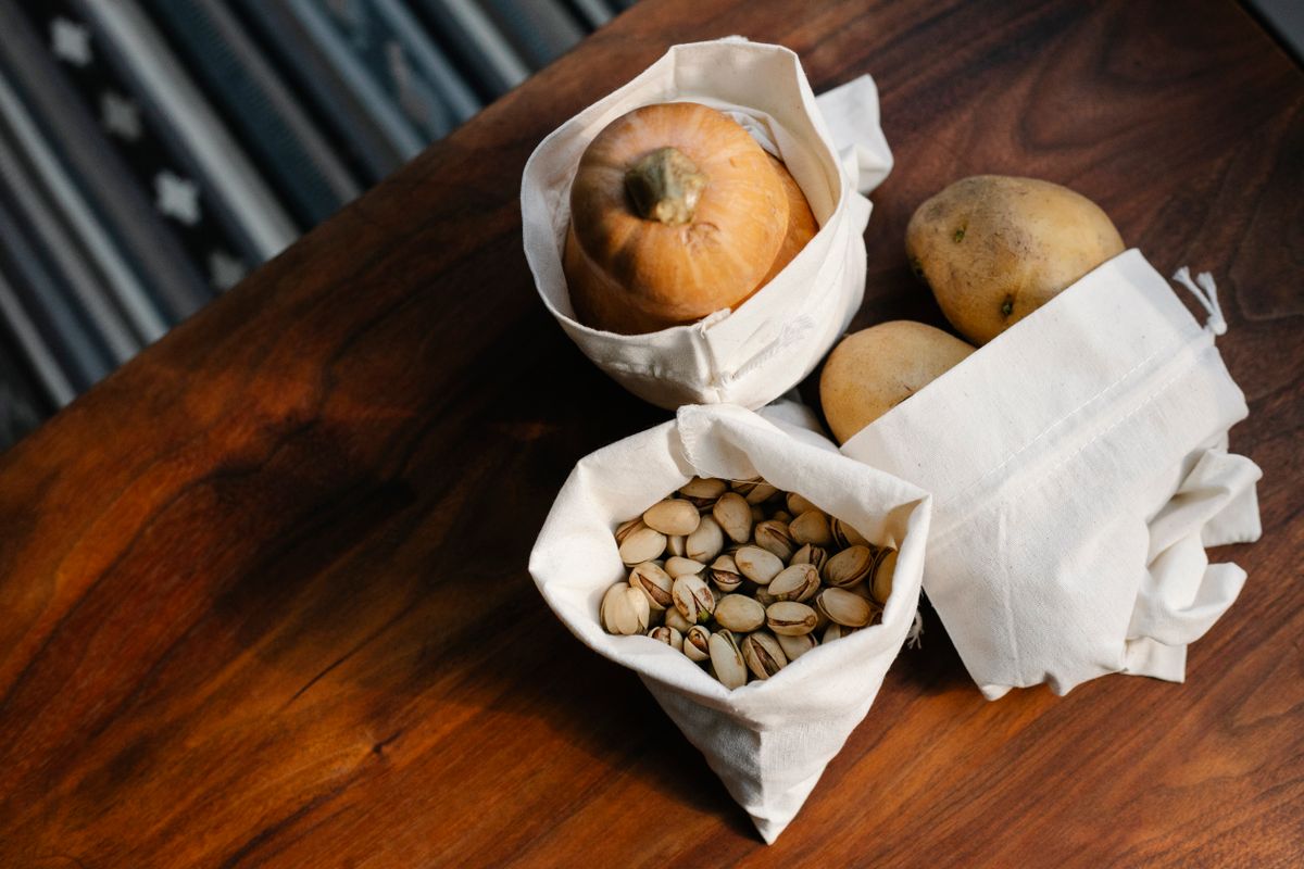 Cotton drawstring bags with organic seeds and natural herbs arranged on a wooden surface, representing the wholesale range of OEKO-TEX certified cotton seed bags produced in India for export to the UK and USA