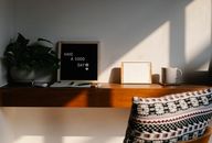 Chair with cushion placed at wooden shelf with Have A Good Day inscription on black board between potted plant and blank notice board with paper
