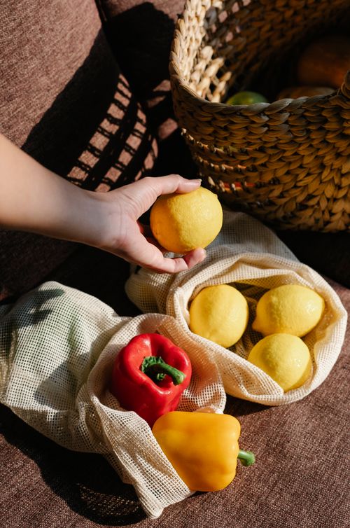 Free From above of crop faceless person with ripe lemon on hand standing near ECO friendly sacks with colorful bell peppers Stock Photo