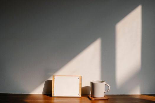Wooden notice board with empty paper near white mug on coaster placed on table near wall in light room at home