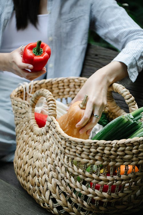 Crop woman putting vegetables into wicker basket