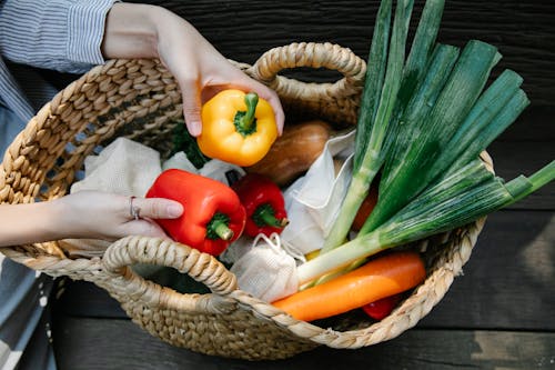 Free Crop unrecognizable woman placing ripe vegetables in wicker basket Stock Photo
