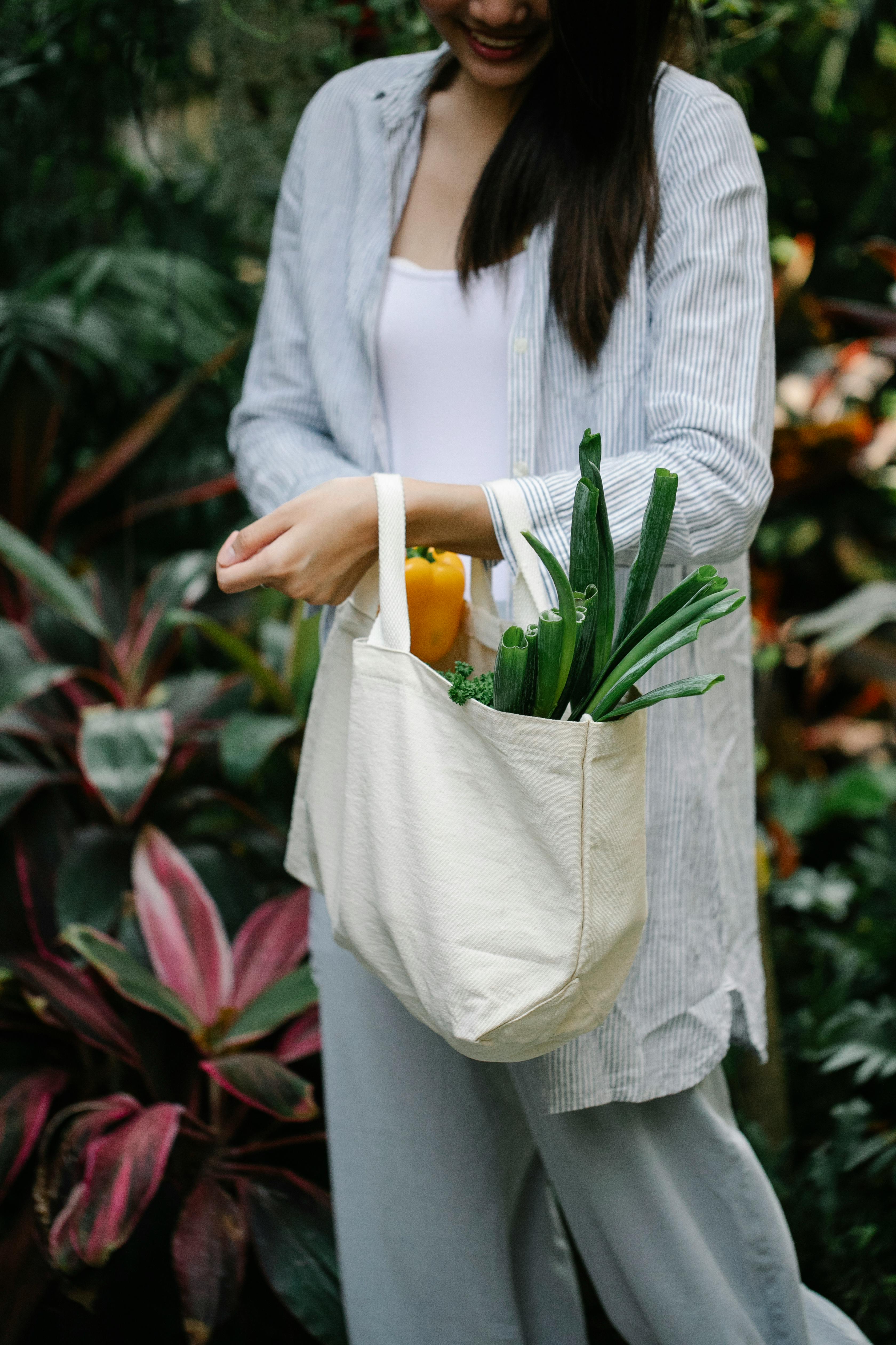 crop smiling woman carrying bag with vegetables in garden