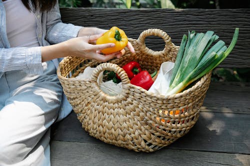 Free Crop unrecognizable woman placing fresh vegetables in basket in garden Stock Photo