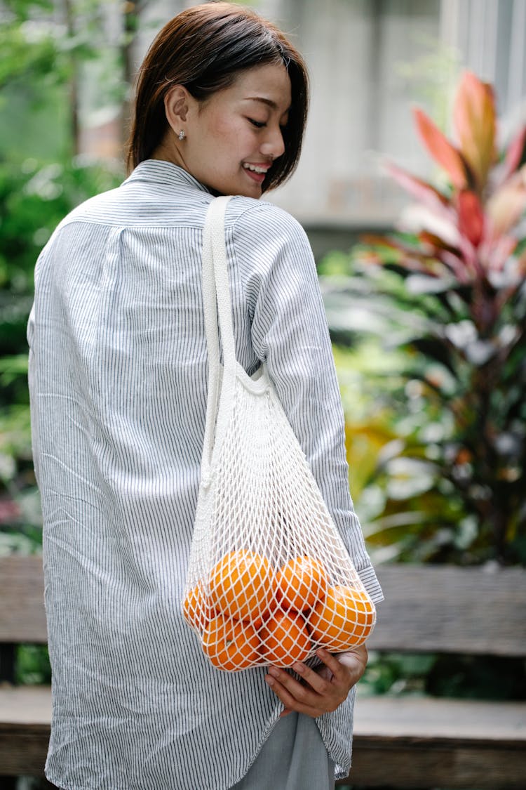 Happy Asian Woman Carrying Bag With Ripe Oranges