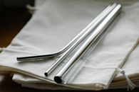 Collection of stainless steel straight and bent straws placed on reusable bags on table