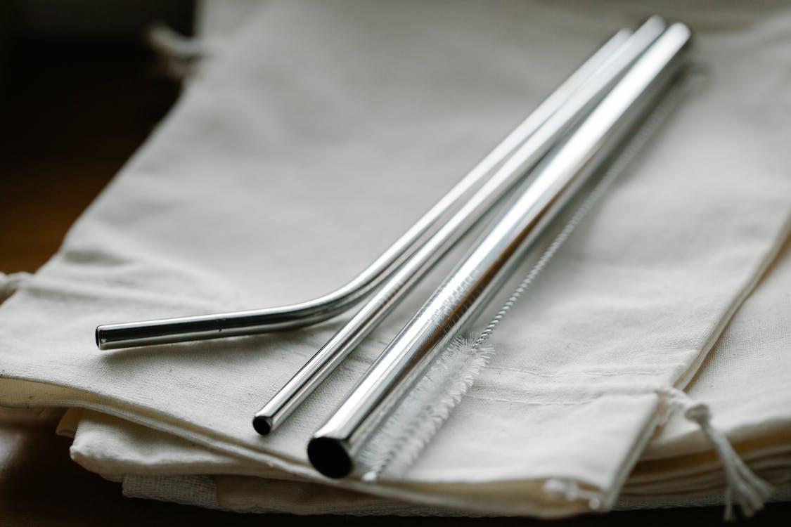 Collection of stainless steel straight and bent straws placed on reusable bags on table