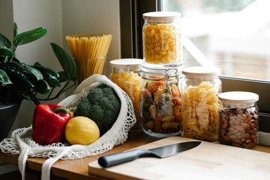 A kitchen countertop with fresh vegetables, assorted pasta jars, and a knife.
