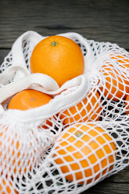Fresh oranges in net bag on wooden surface