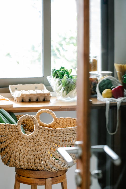 Wicker basket placed on stool near counter with eggs and vegetables in light kitchen