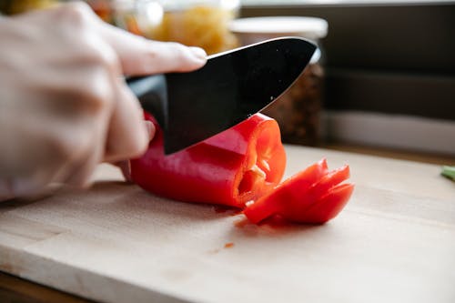 Crop faceless chef cutting ripe red bell pepper on chopping board in light kitchen