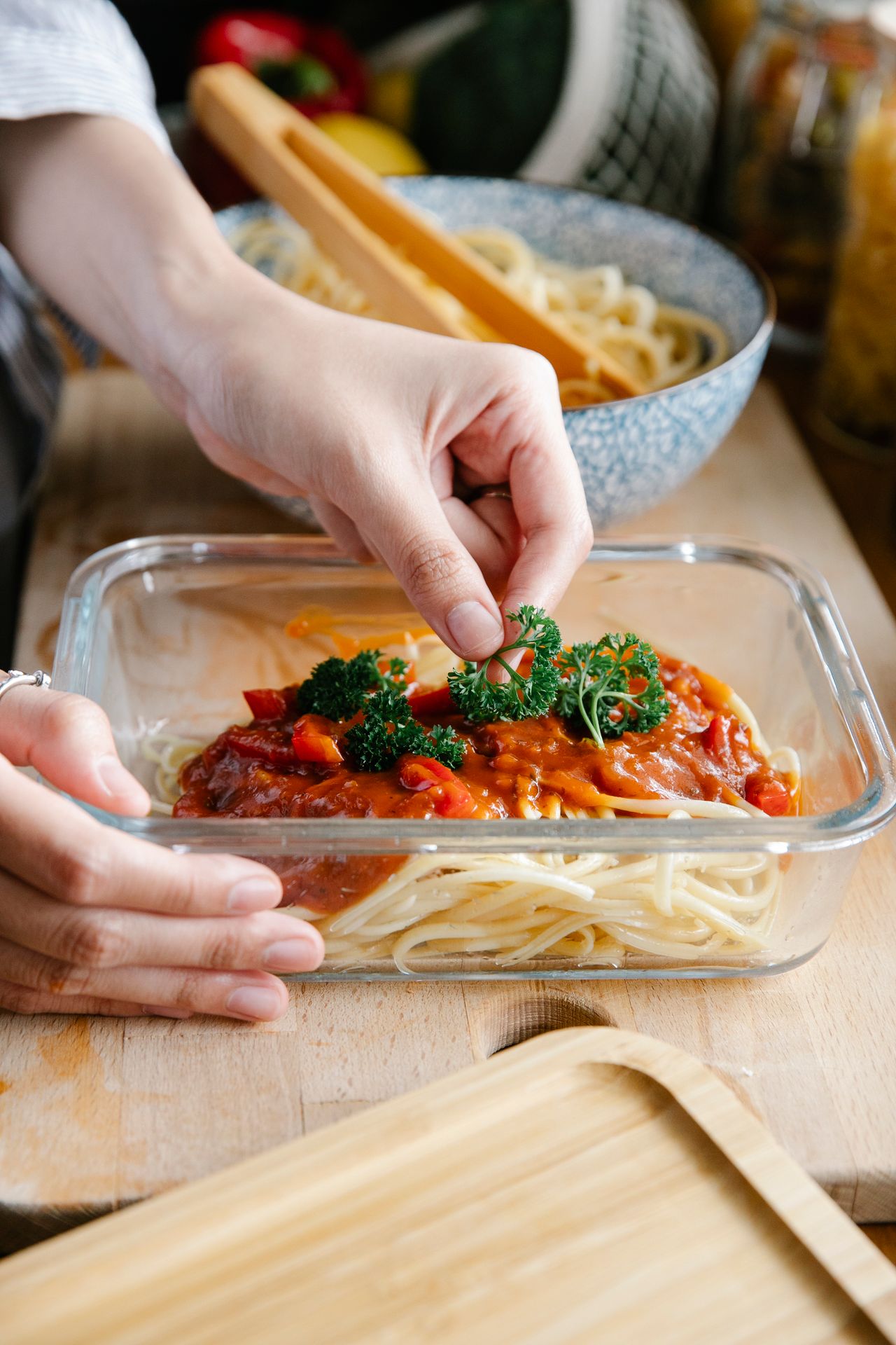 Hands garnishing a dish of spaghetti with tomato sauce and fresh parsley